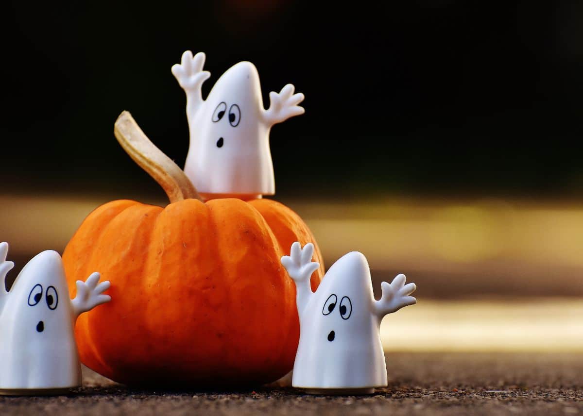 Three toy ghosts are sitting on a buy a small pumpkin outside.