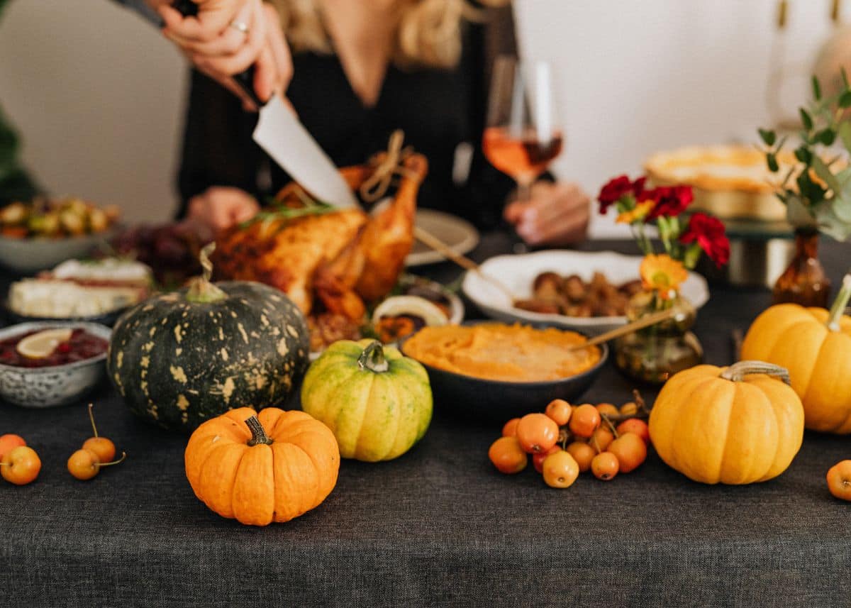 A table with Thanksgiving dinner and a woman is carving the turkey.