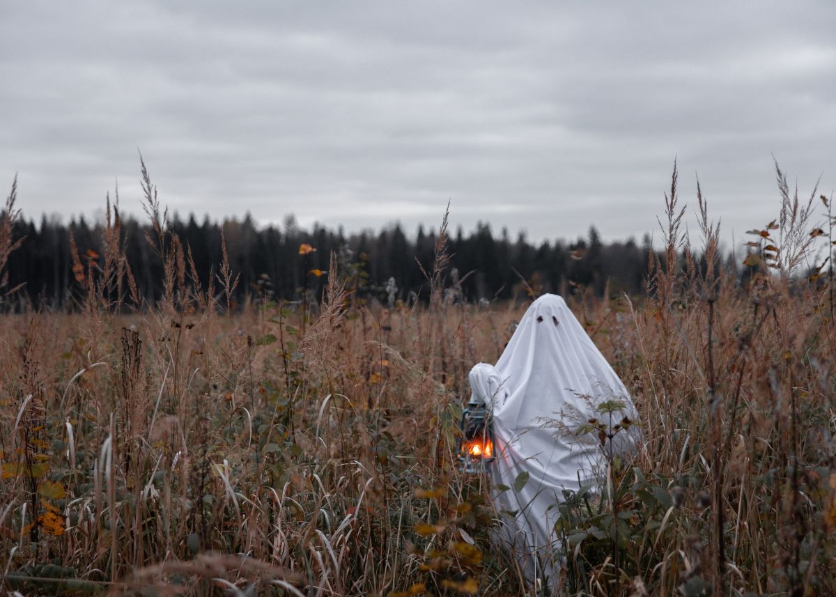 Someone dressed up like a ghost is carrying a lantern in a f