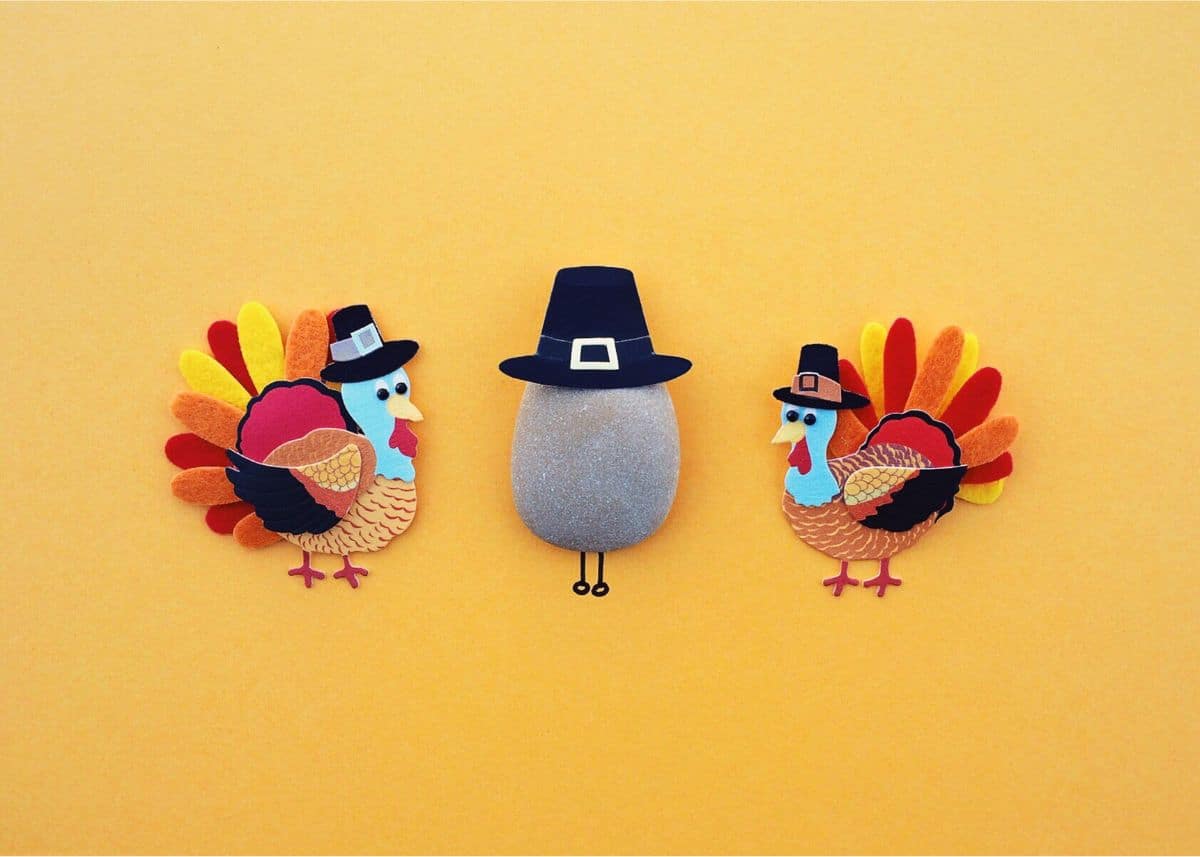 This is a photo of two felt turkeys wearing Pilgrim hats. There is a rock in the middle with a Pilgrim hat.
