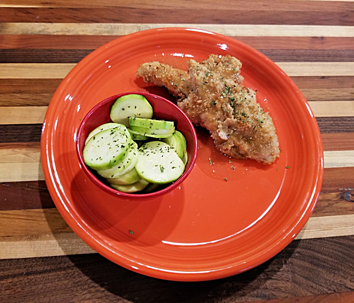 air fried chicken finger on an orange plate with a side dish of zucchini